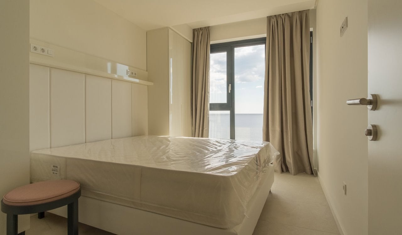 Bedroom in an apartment in Becici, Montenegro: light finishes, a double bed, and a panoramic window with sea view.