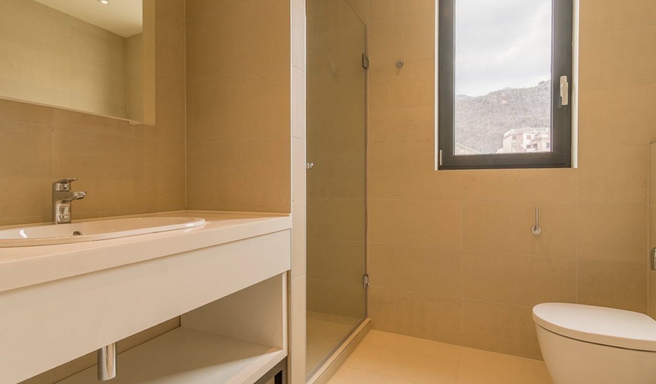 Modern bathroom with a shower cabin in an apartment in Bečići, Montenegro: beige tiles and mountain view.