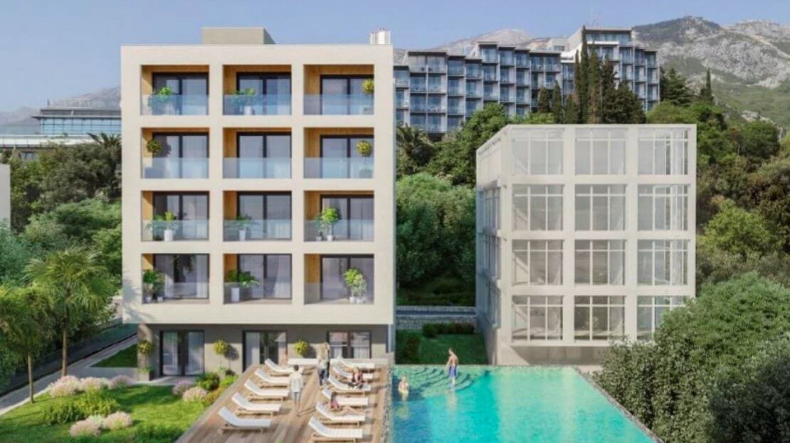 Modern residential complex with a pool and terrace in Bečići, Montenegro: view of the building with panoramic windows and mountains.