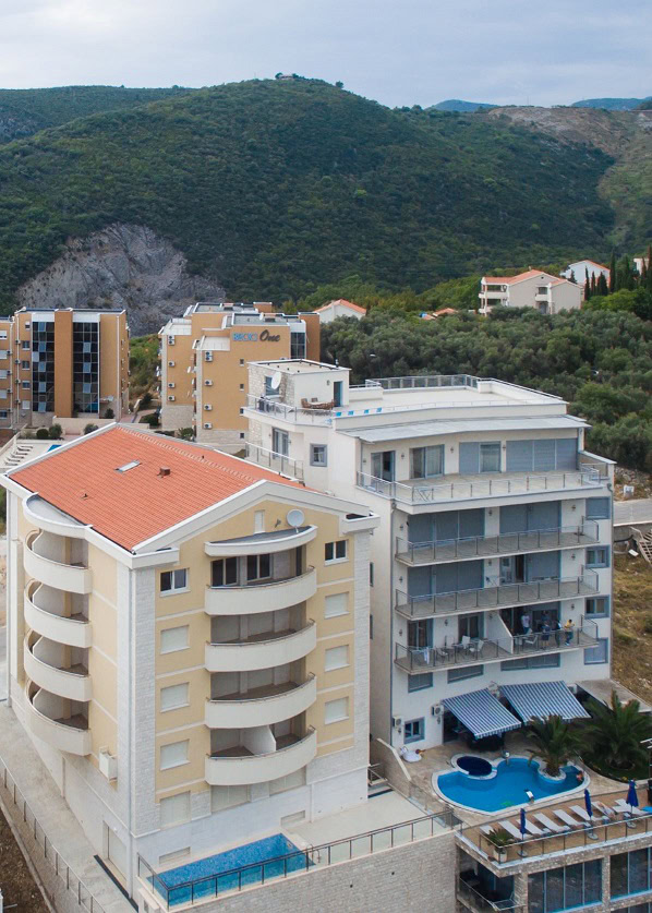 Modern residential complexes with pools in Bečići, Budva Riviera, Montenegro: view of buildings and mountains.