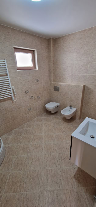 Modern bathroom in an apartment in Bečići, Montenegro: wall-mounted toilet, bidet, beige tiles, and a window.