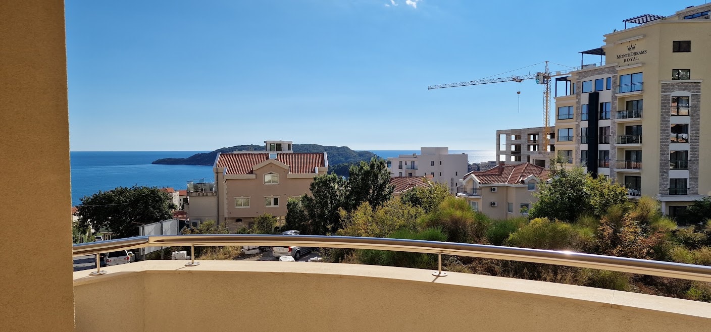 View from the apartment balcony in Bečići, Montenegro: a panorama of the Adriatic Sea, surrounding buildings, and greenery.