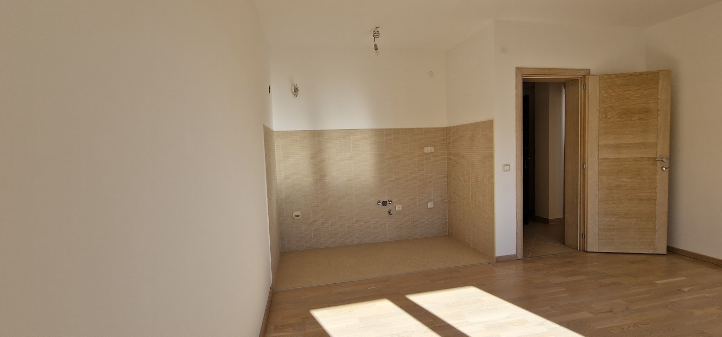 Kitchen area in an apartment in Bečići, Montenegro: light finishes, tiled backsplash, parquet flooring, and an interior door.