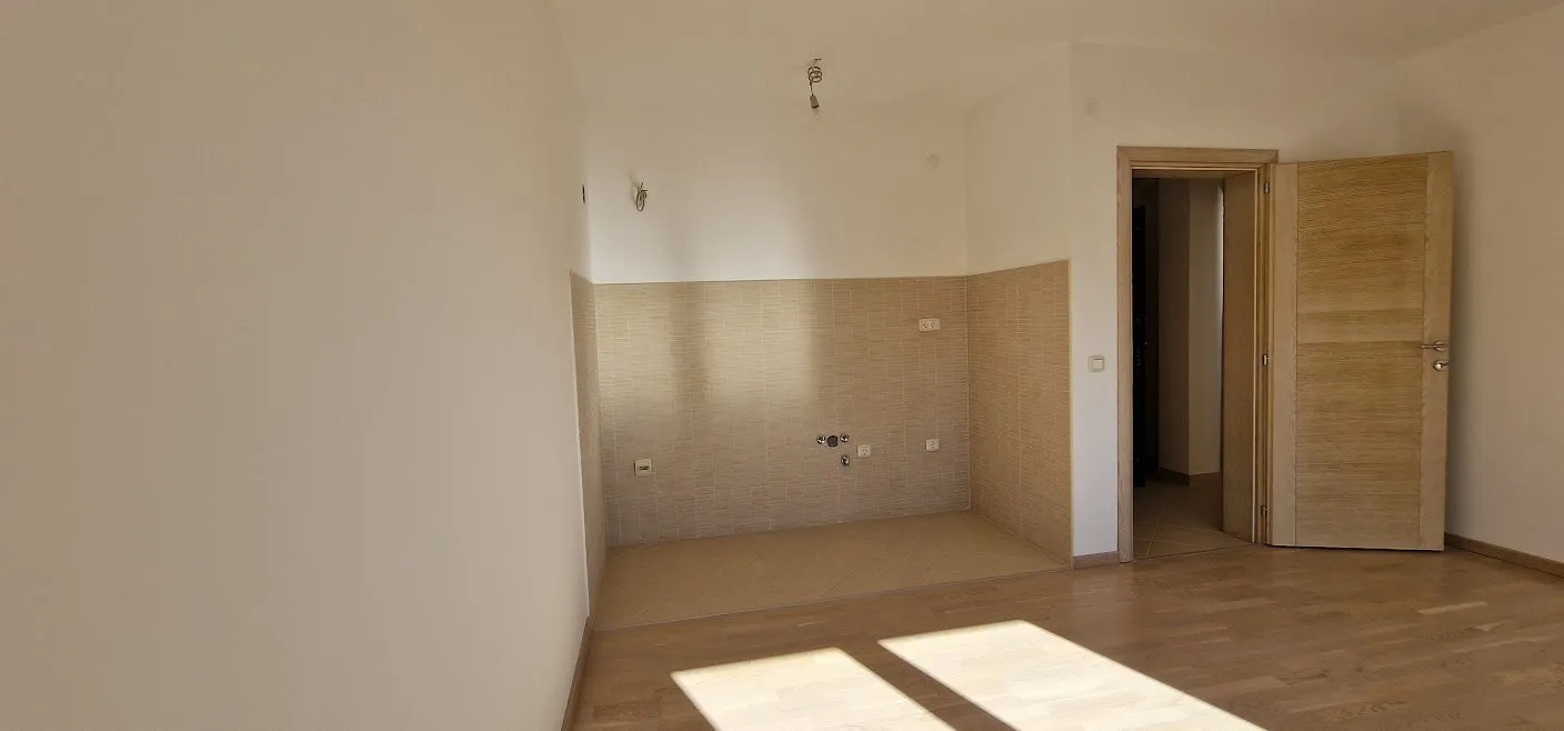 Empty room with wood flooring and a beige tiled wall section featuring plumbing outlets and electrical sockets.
