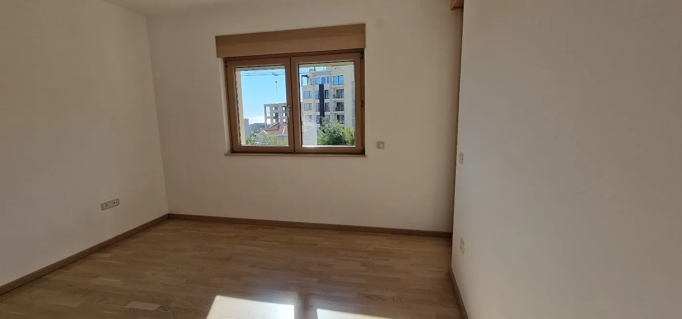 Empty room with laminate flooring and a window overlooking buildings. No furniture or specific room features visible.