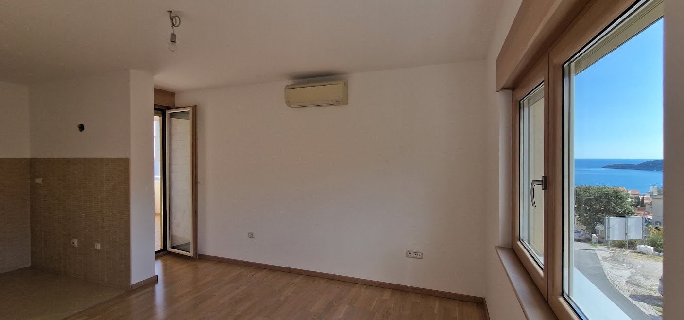 Bright living room in an apartment in Bečići, Montenegro: parquet flooring, air conditioning, and a panoramic sea view from the window.