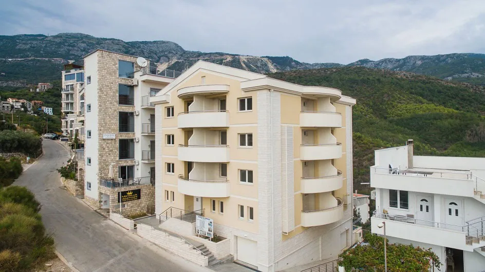 Exterior view of a multi-story residential building with balconies and stone facade against mountains.