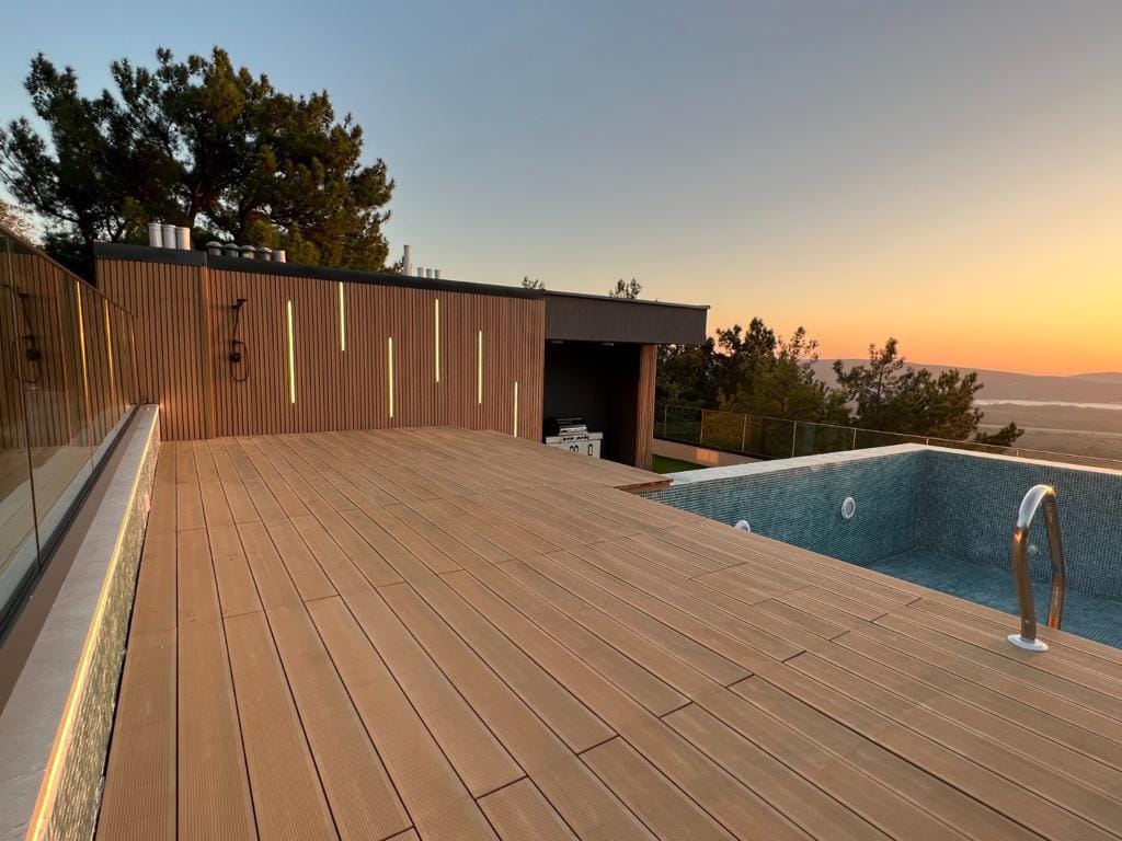 Villa terrace in Kavac, Montenegro: wooden decking, illuminated pool, and panoramic sunset view.