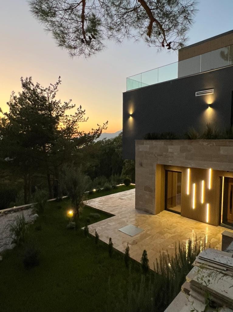 Modern villa in Kavac, Montenegro: illuminated facade, stone cladding, terrace, and sunset view in the garden.