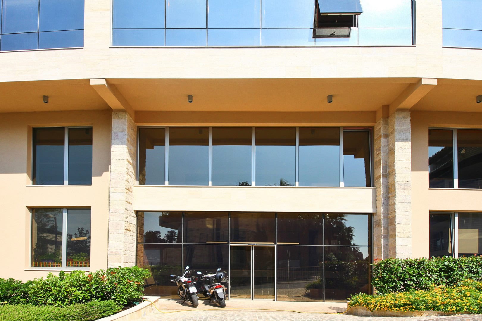 Facade of the Harmonia business center in Budva, Montenegro: panoramic glazing, entrance area, and motorcycle parking.