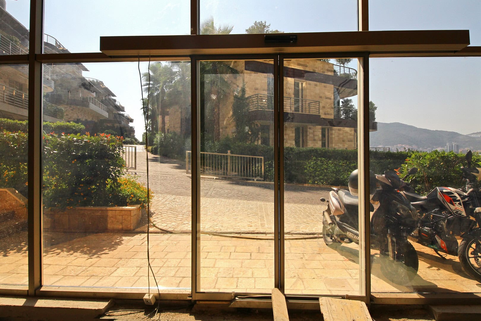 View from the panoramic windows of the Harmonia commercial space in Budva, Montenegro, onto the landscaped grounds and parking area.