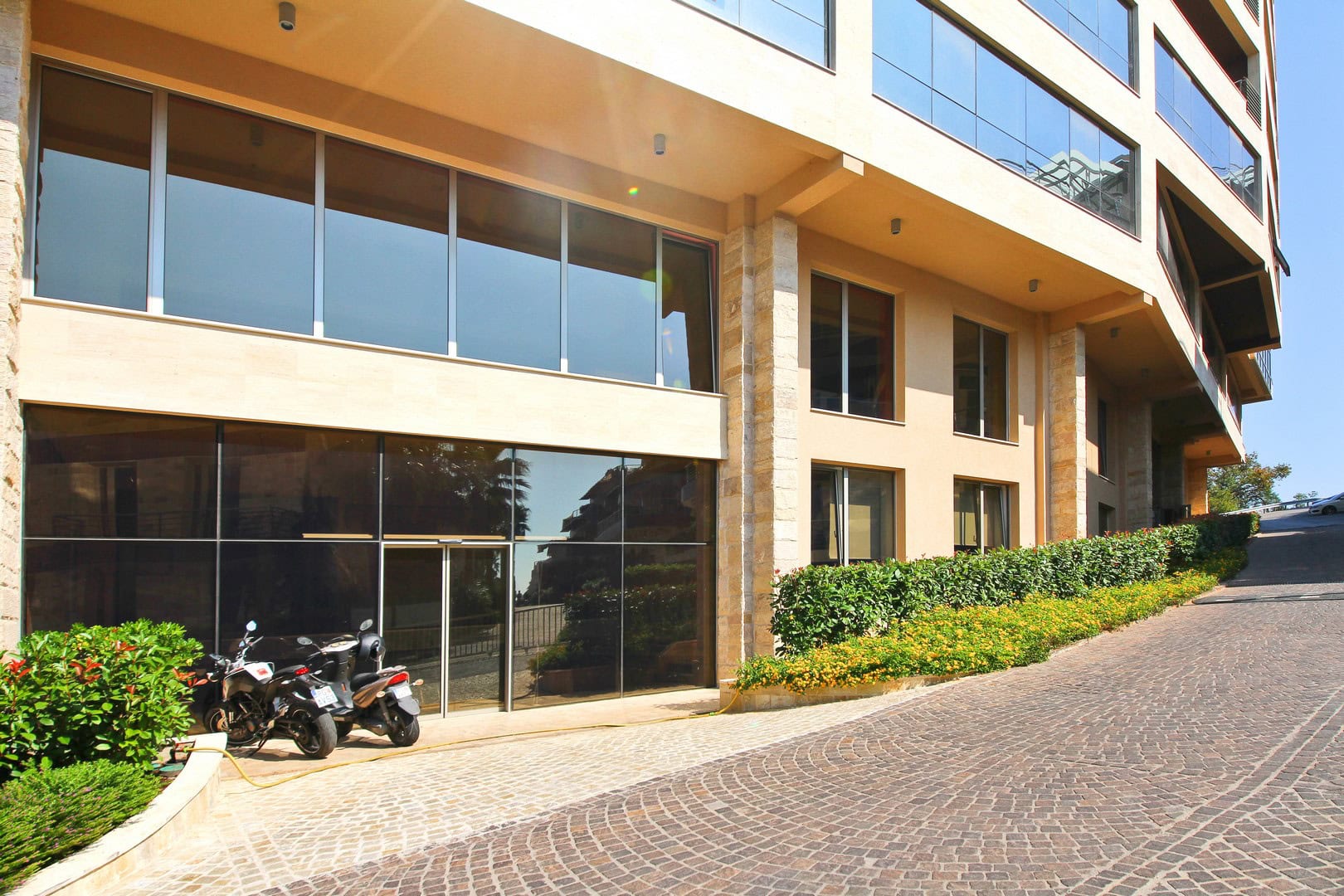 Facade of the modern Harmonia business center in Budva, Montenegro, with panoramic glazing and a paved driveway.