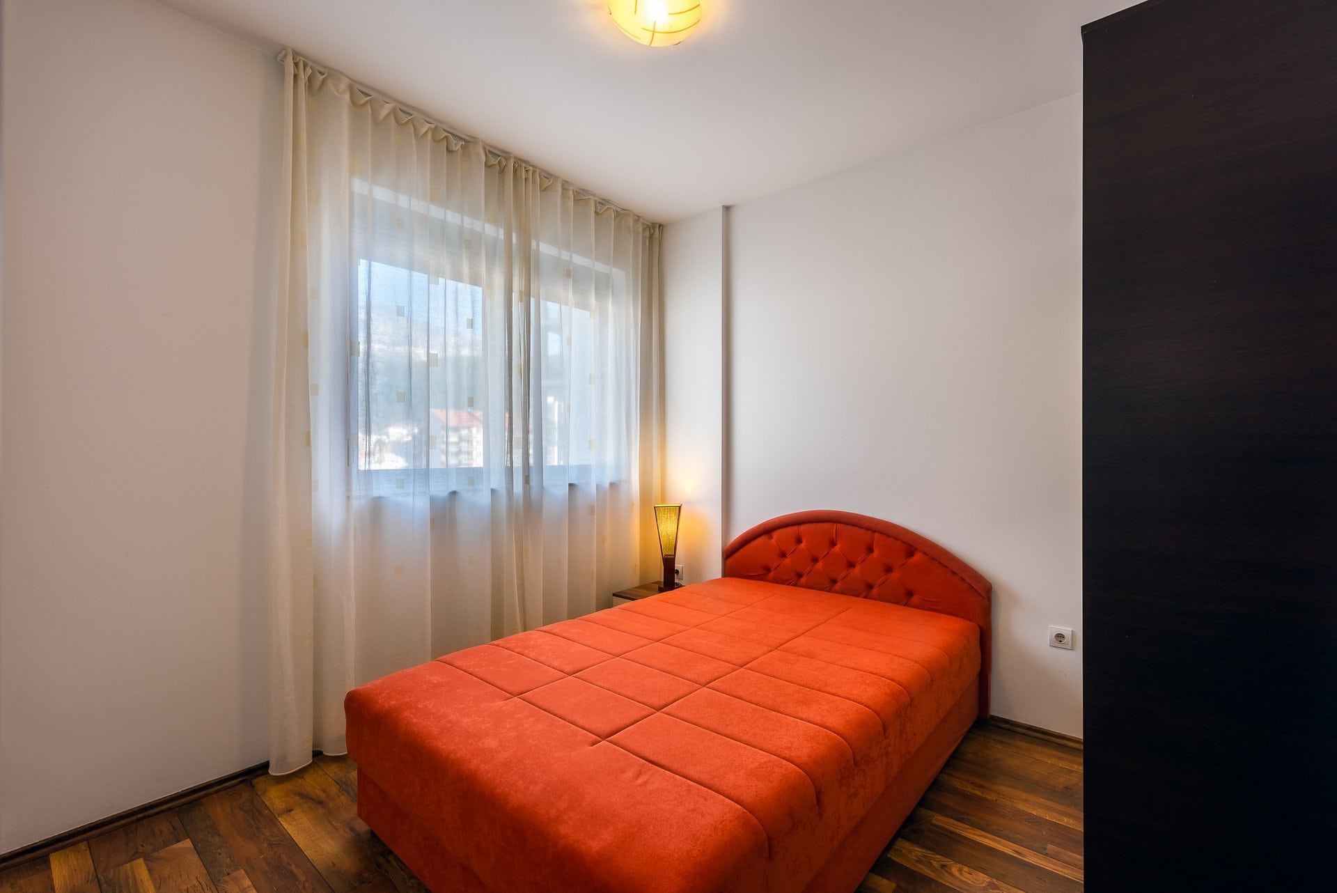 Cozy bedroom with a bright red bed and parquet flooring in an apartment in Budva, Montenegro.