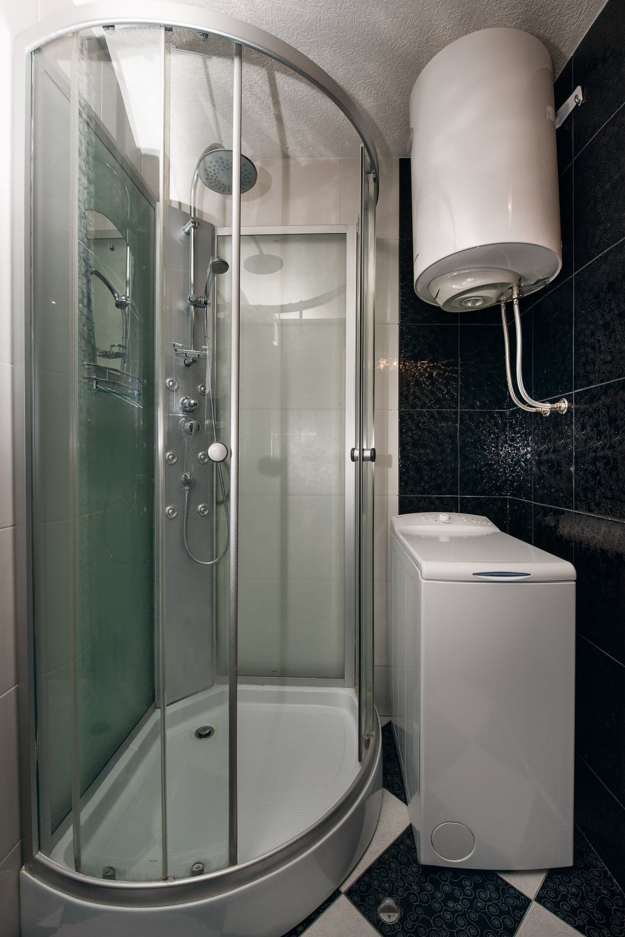 Bathroom in an apartment in Budva, Montenegro: shower cabin, washing machine, and water heater, black tiles.