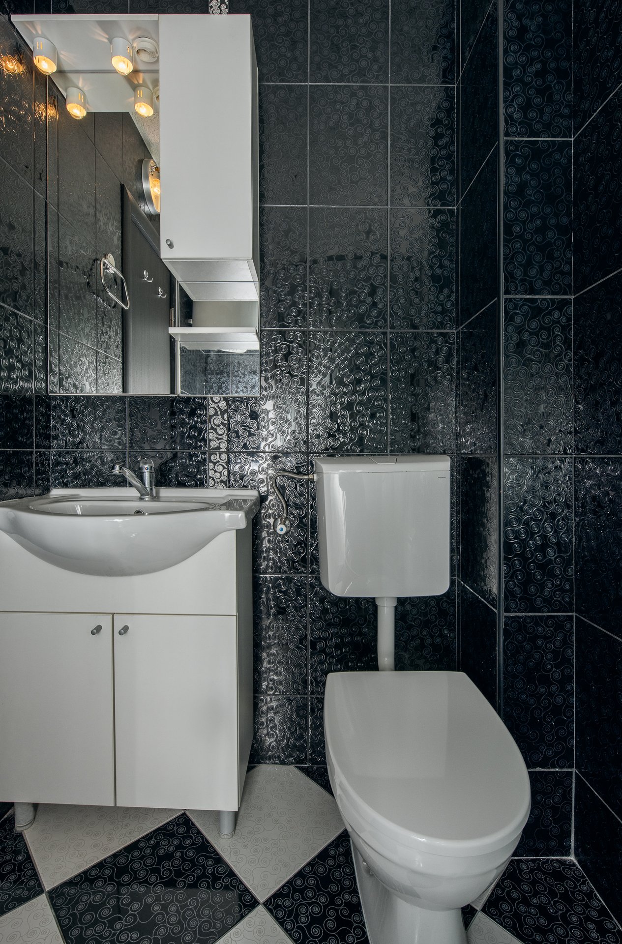 Bathroom in an apartment in Budva, Montenegro: white fixtures, mirrored cabinet, and black patterned tile.