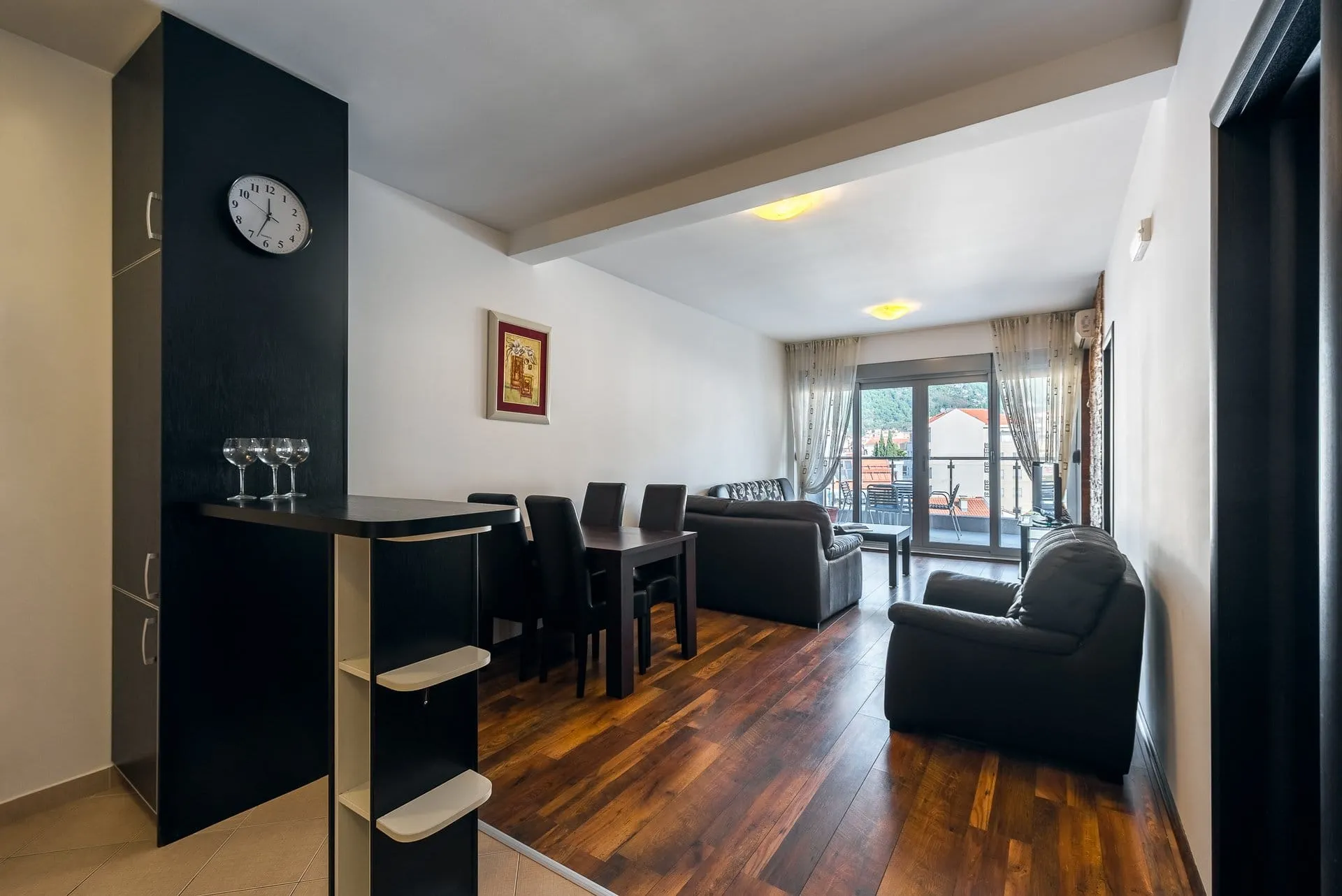 Living room with dark sofa, dining table, bar counter, and wooden flooring.