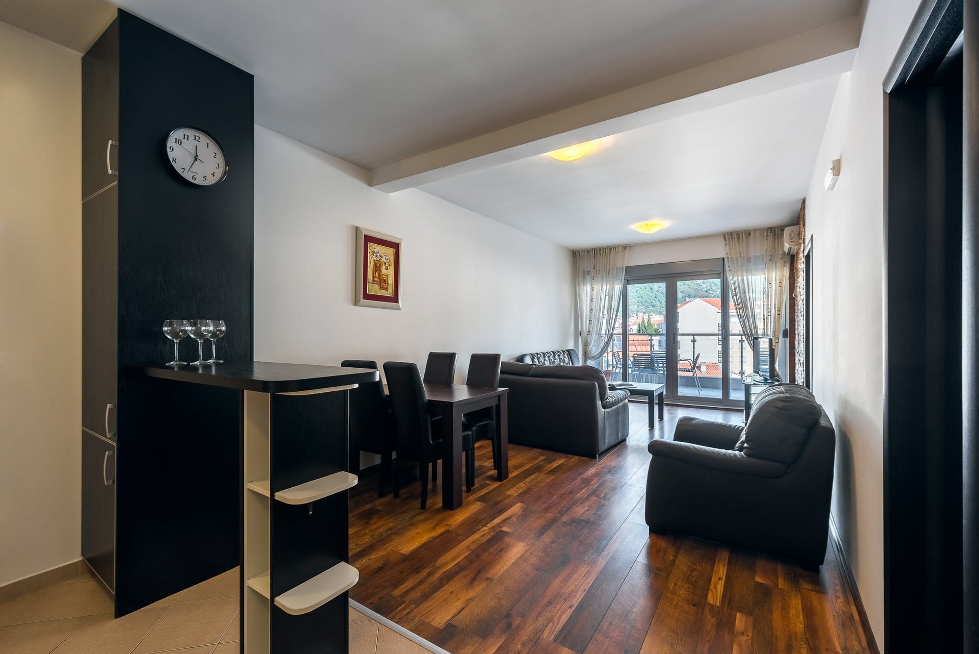 Living room with dark furniture, dining area, and access to the balcony in an apartment in Budva, Montenegro.