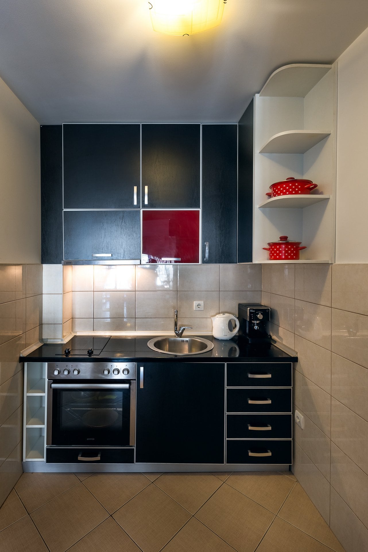 Compact kitchen in an apartment in Budva, Montenegro: black cabinetry, built-in appliances, tile, and open shelves.