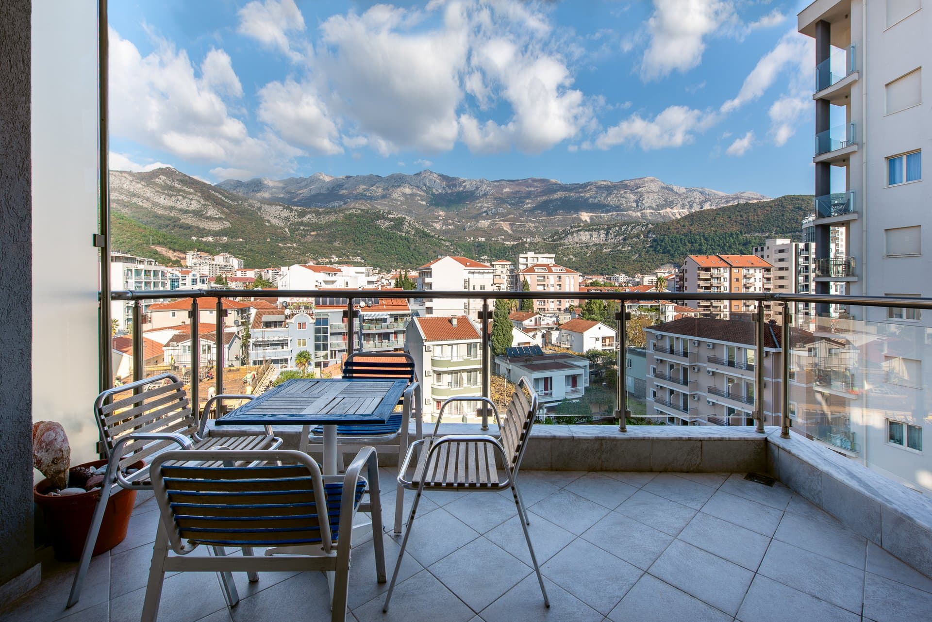 Balcony with furniture and panoramic views of the mountains and the city of Budva, Montenegro. Apartment with a terrace and glass railing.