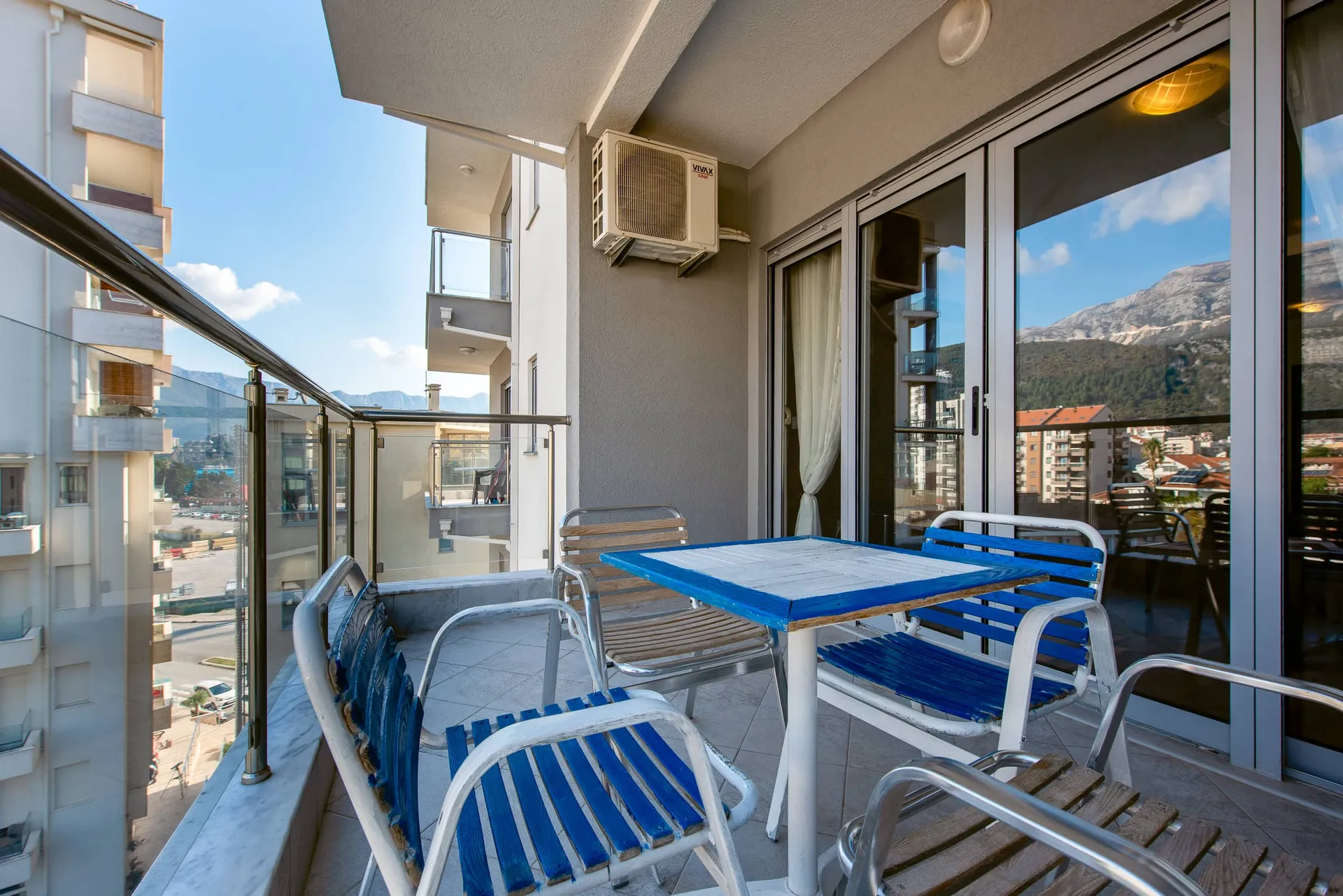 Balcony with blue outdoor furniture, glass railing, and wall-mounted air conditioner unit.