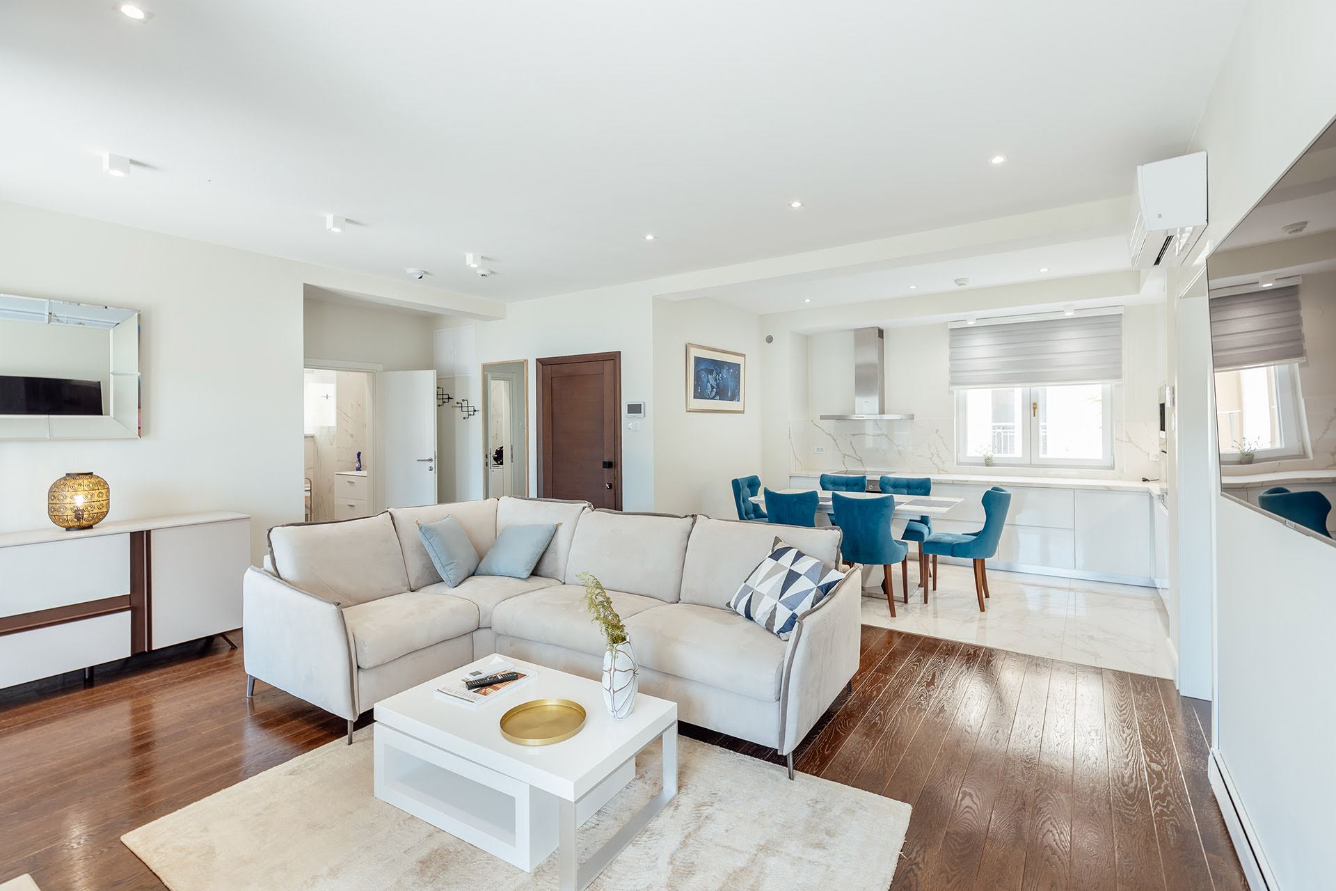 Modern living room with a beige sofa and kitchen in a residential complex in Kumbor, Montenegro: stylish interior, parquet flooring, and light-colored furniture.