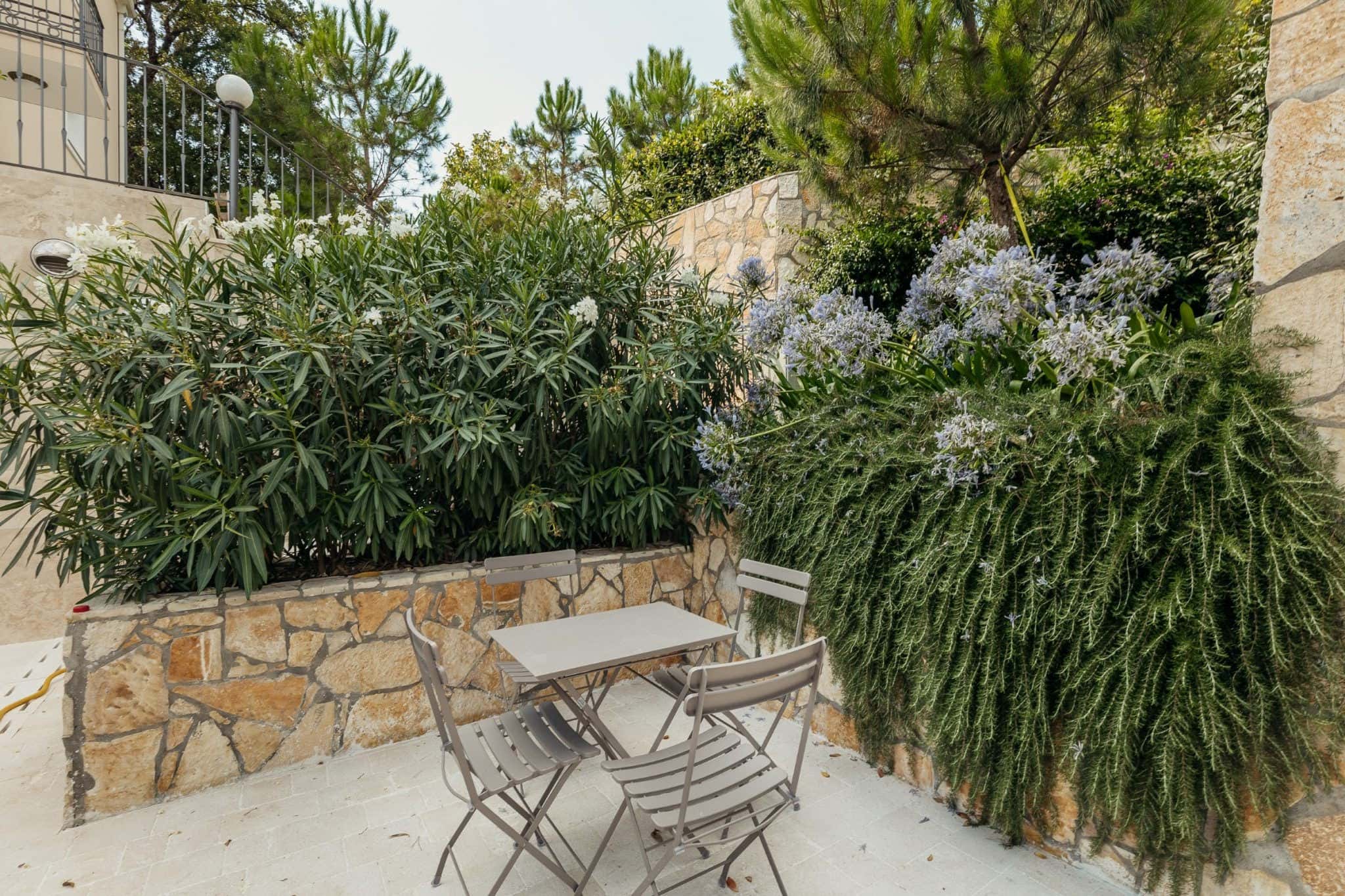 Cozy terrace with garden furniture in a residential complex in Kumbor, Montenegro, among a blooming garden and stone walls.