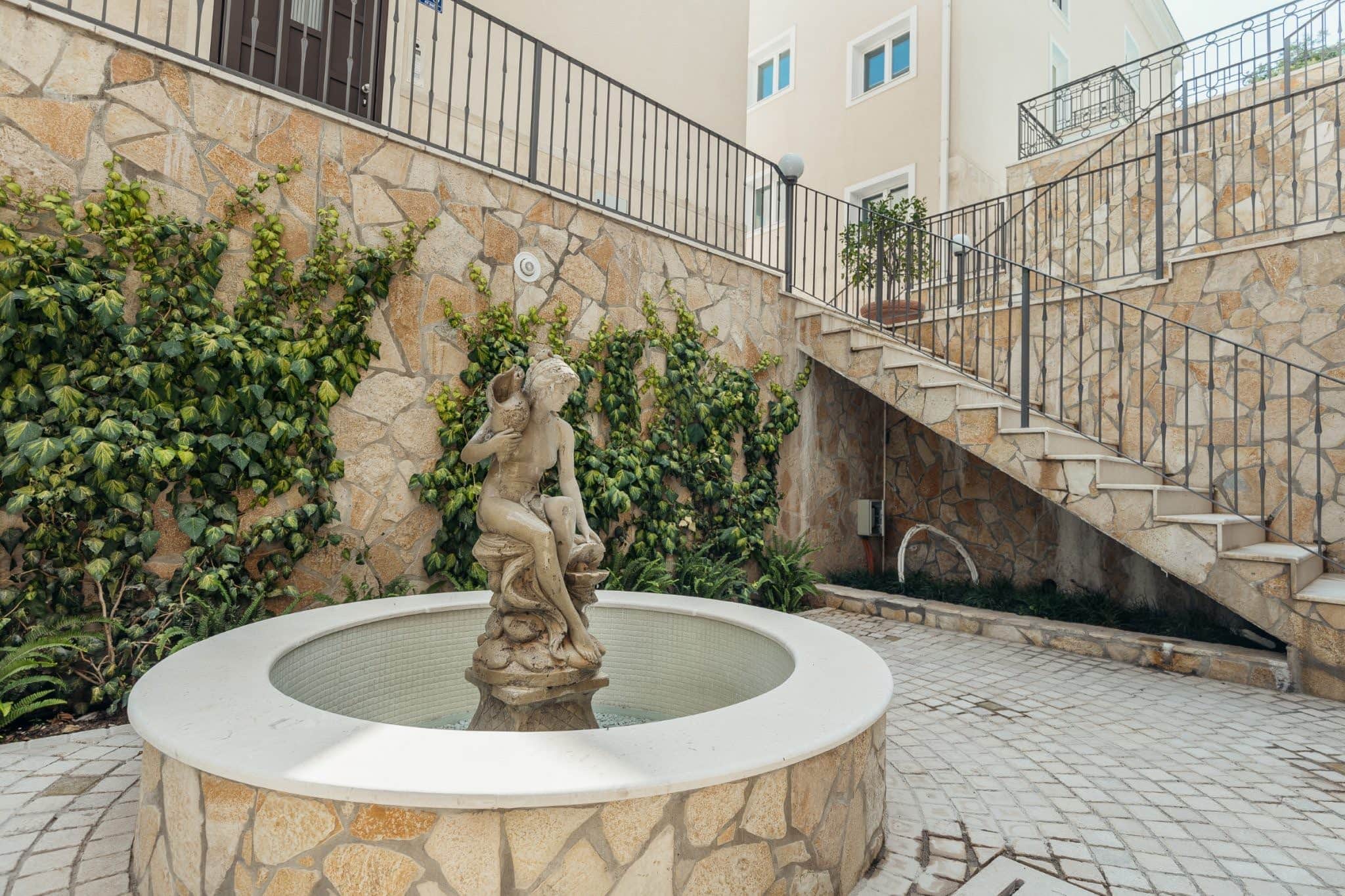 A fountain with a statue and a stone staircase in the courtyard of a residential complex in Kumbor, Montenegro.