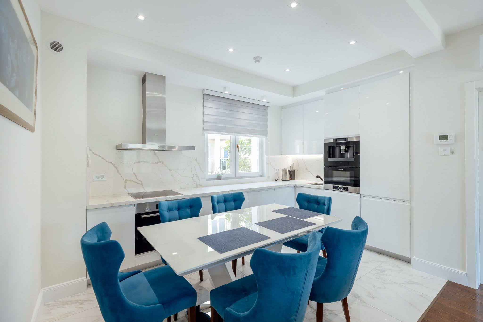 Modern kitchen with white cabinetry and blue chairs in a residential complex in Kumbor, Montenegro.
