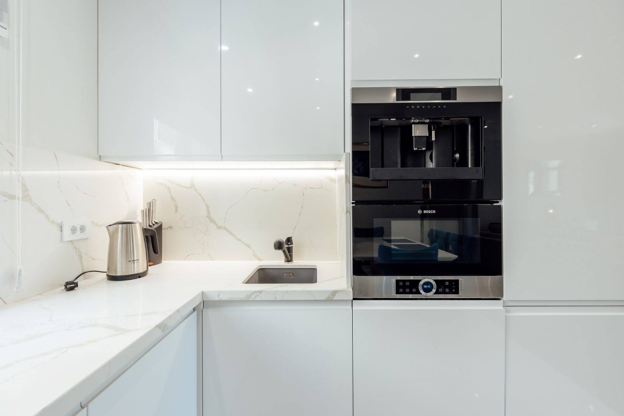 Modern white kitchen with Bosch and AEG appliances in a residential complex, Kumbor, Montenegro: marble countertop and lighting.