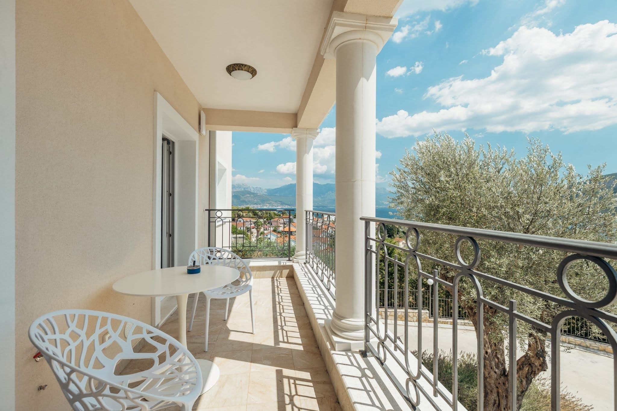 Balcony with columns and sea view in a residential complex in Kumbor, Montenegro: white furniture and wrought-iron railing.