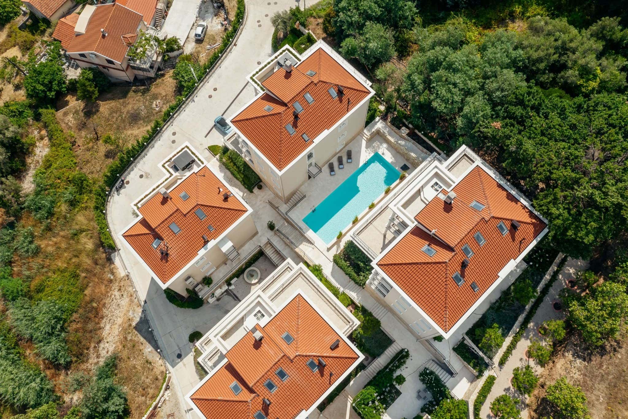 Aerial view of a residential complex in Kumbor, Montenegro: villas with red tile roofs, a swimming pool, and landscaped grounds.