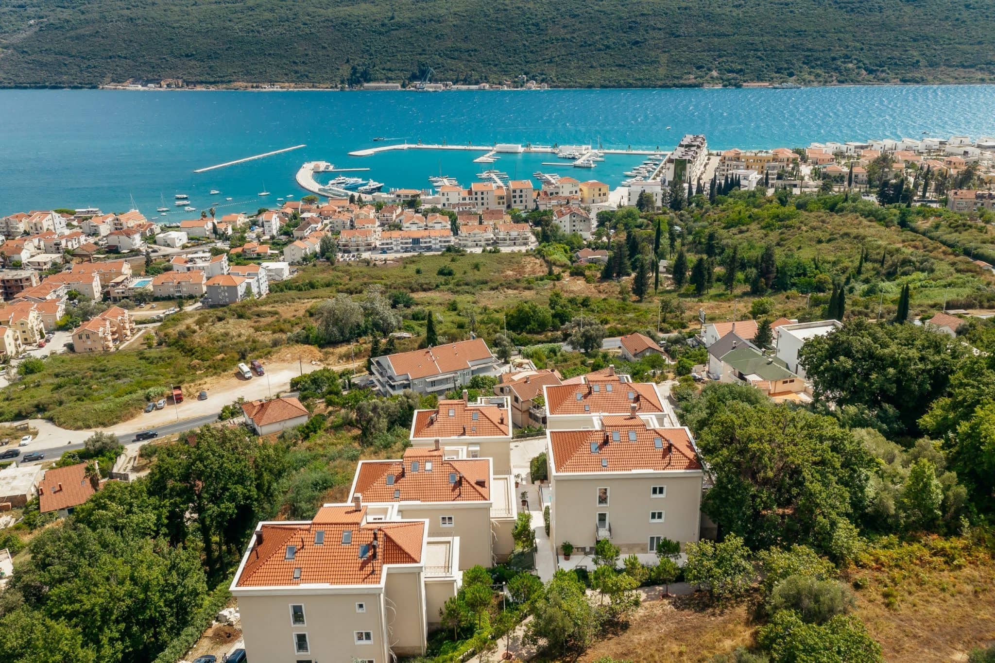 Aerial view of a residential complex in Kumbor, Montenegro: modern houses with tiled roofs and a sea panorama.