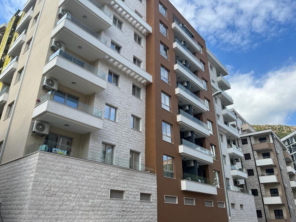 Modern residential complex in Bečići, Montenegro: the facade of a new building with balconies, panoramic windows, and stone cladding.