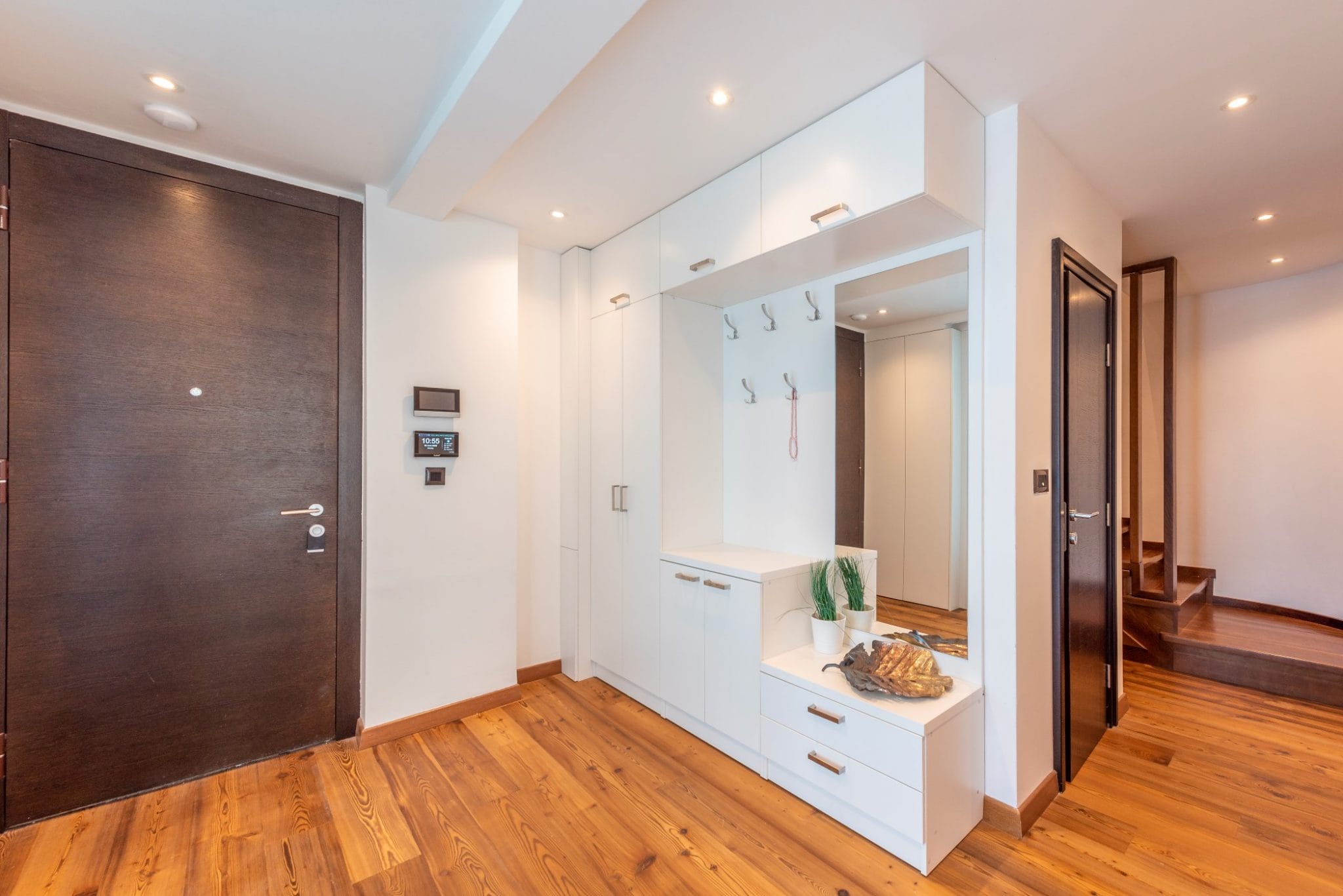 Modern entryway in a penthouse in Bečići, Montenegro: white wardrobe with mirror, dark doors, and parquet flooring.