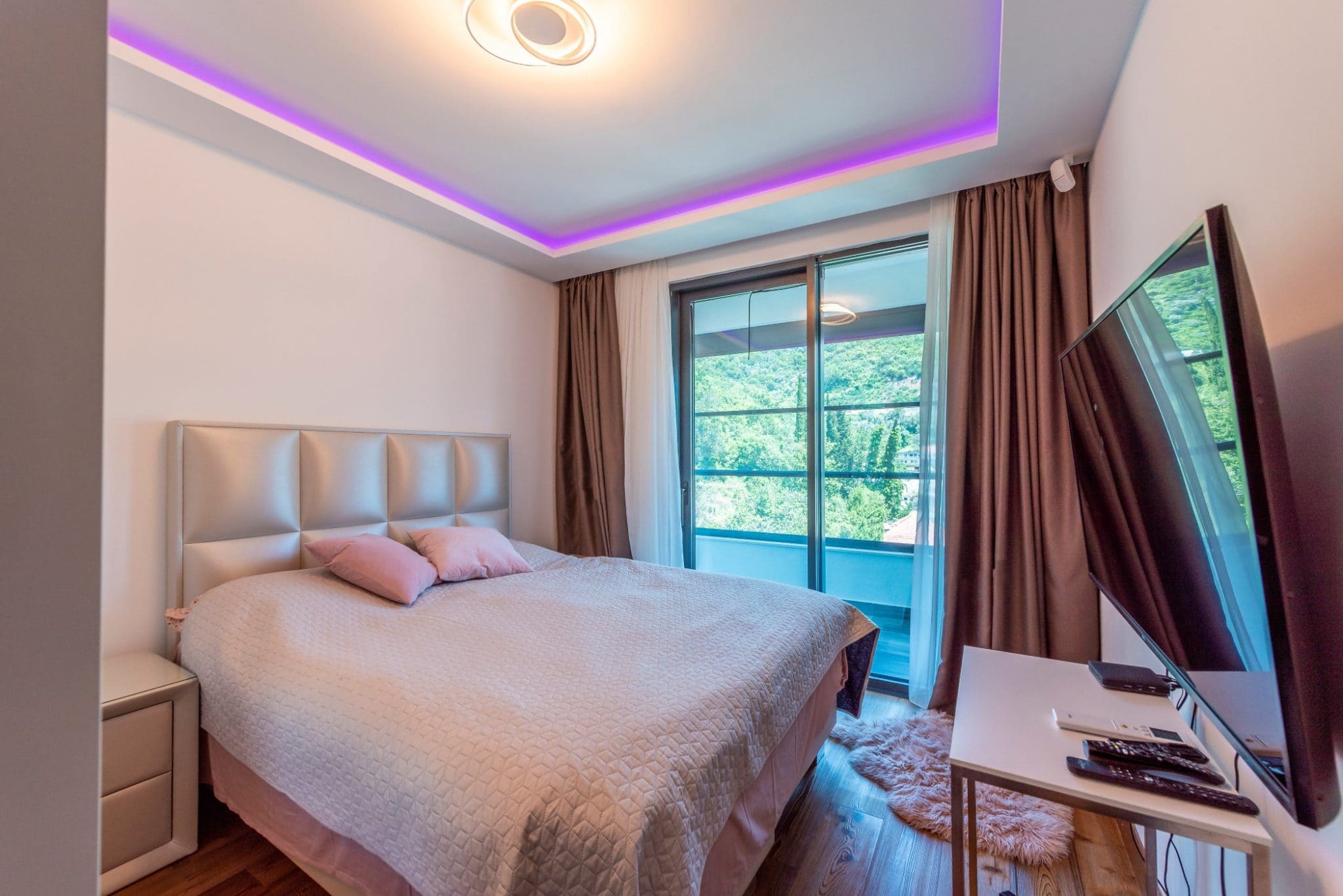 Modern bedroom in a penthouse in Becici, Montenegro: double bed, panoramic window with mountain view, and LED lighting.