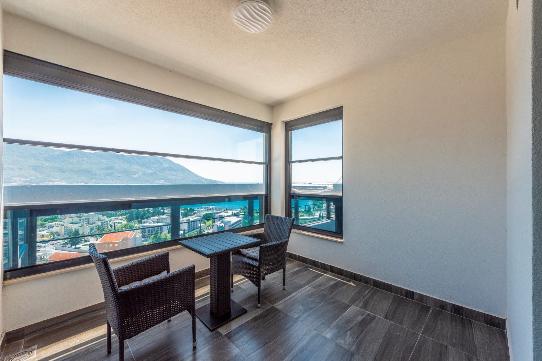 Penthouse balcony in Bečići, Montenegro: panoramic sea view, wicker furniture, and tiled flooring in a modern apartment.