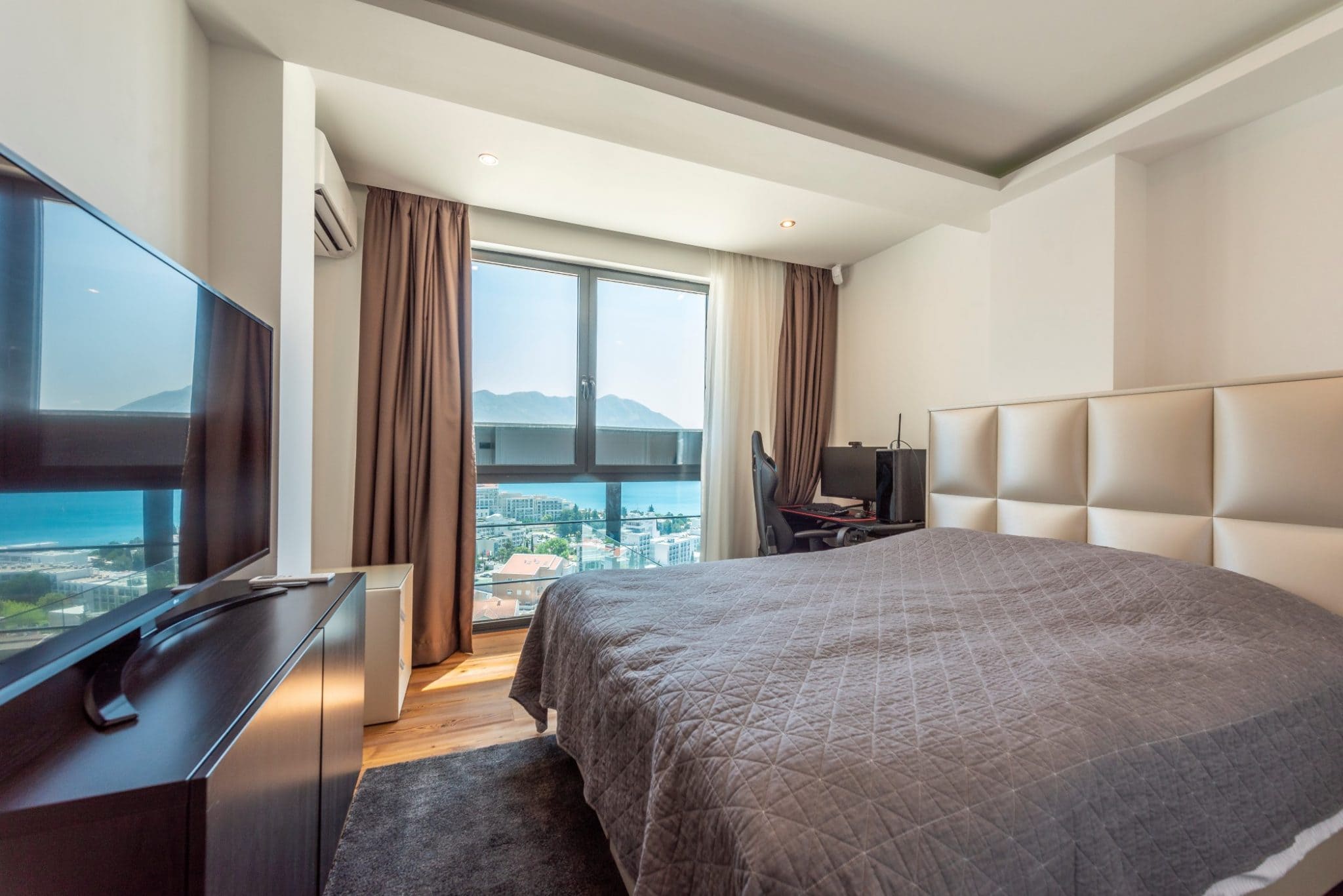 Bedroom in a penthouse in Bečići, Montenegro: a double bed, a workspace, and panoramic views of the sea and mountains.