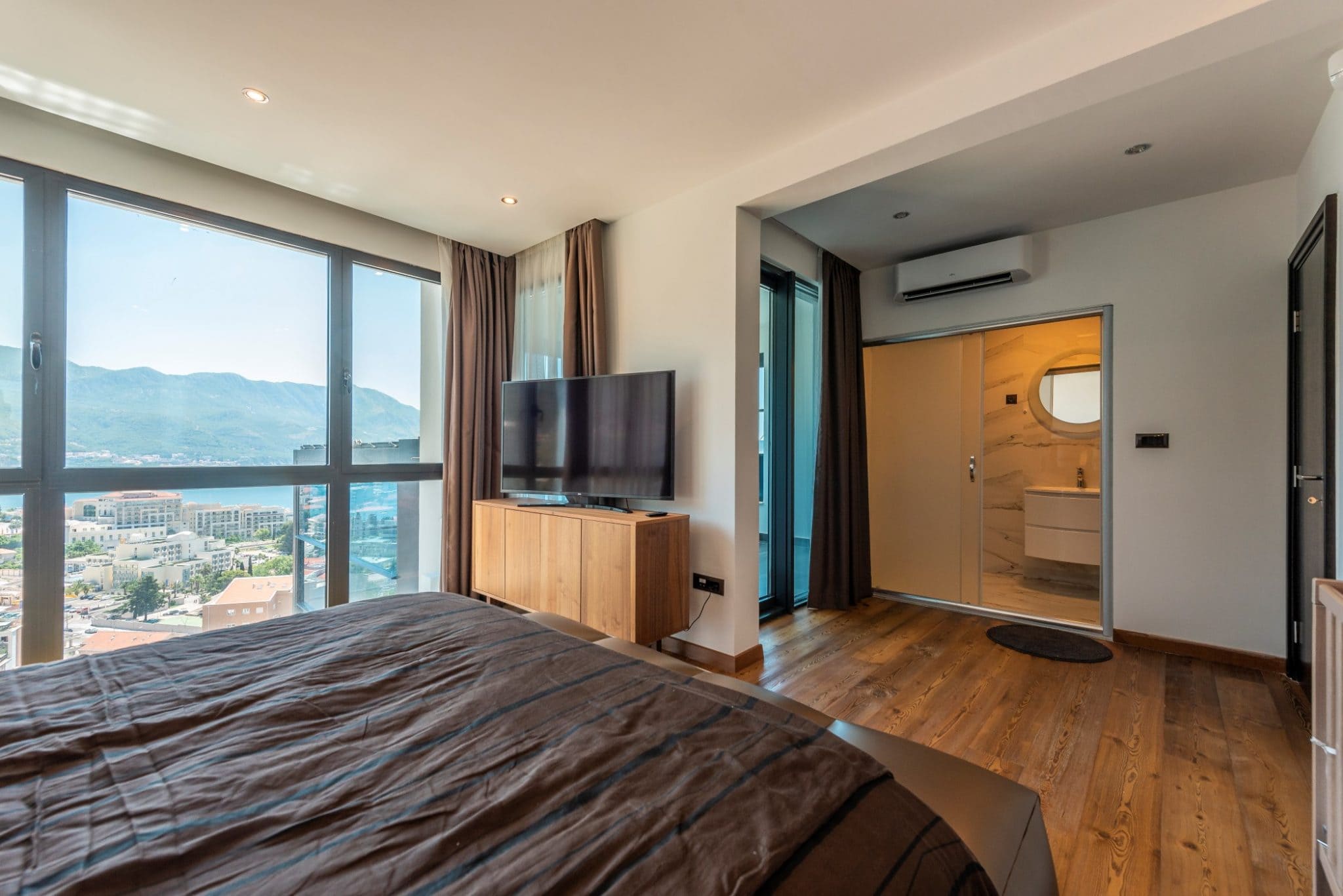 Penthouse bedroom in Bečići, Montenegro: panoramic sea view, modern furniture, and a private bathroom.