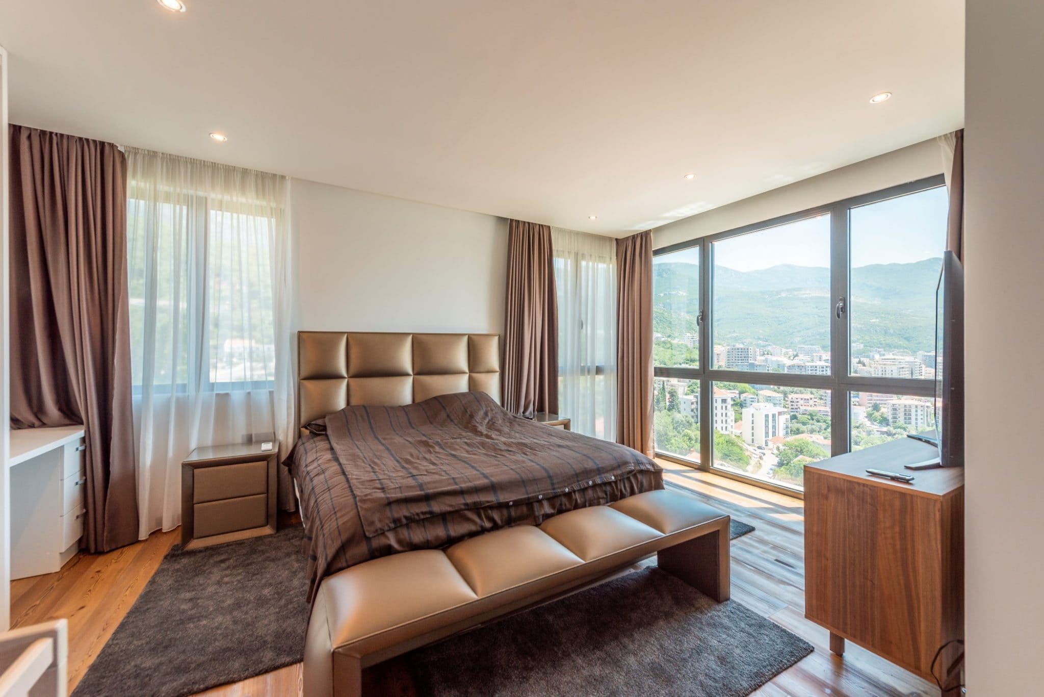 Bedroom in a penthouse in Bečići, Montenegro: a double bed, panoramic windows with mountain and city views.