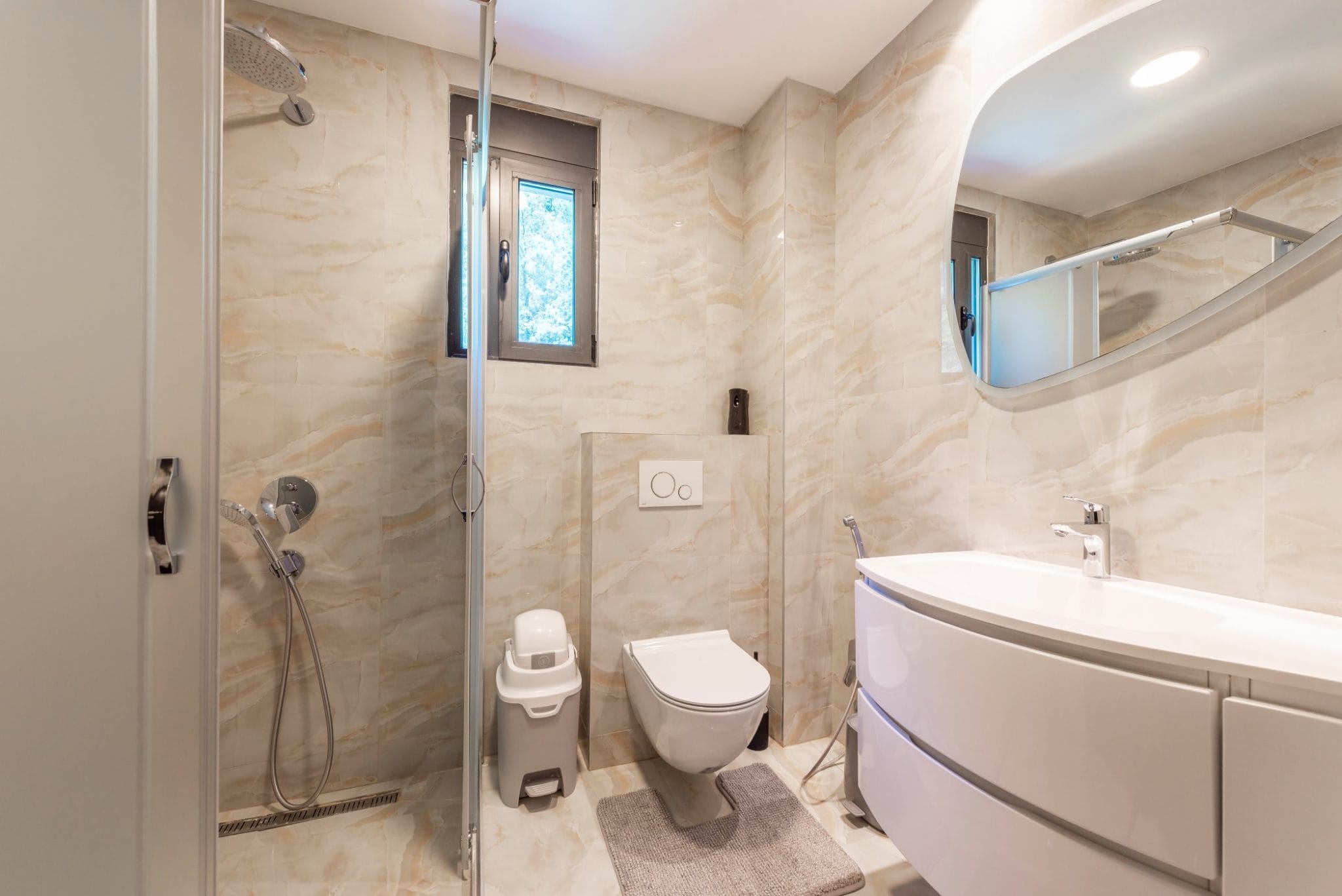 Modern bathroom in a penthouse, Becici, Montenegro: shower cabin, wall-hung toilet, and vanity with sink.