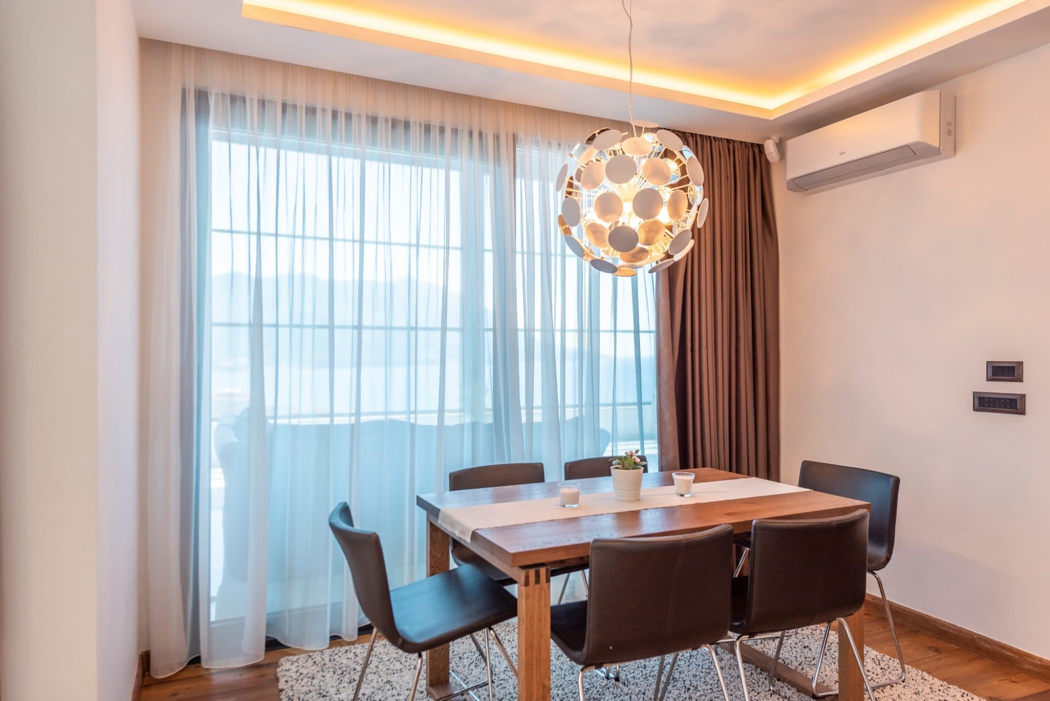 Dining area in a penthouse in Becici, Montenegro: wooden table, designer chandelier, and panoramic window.