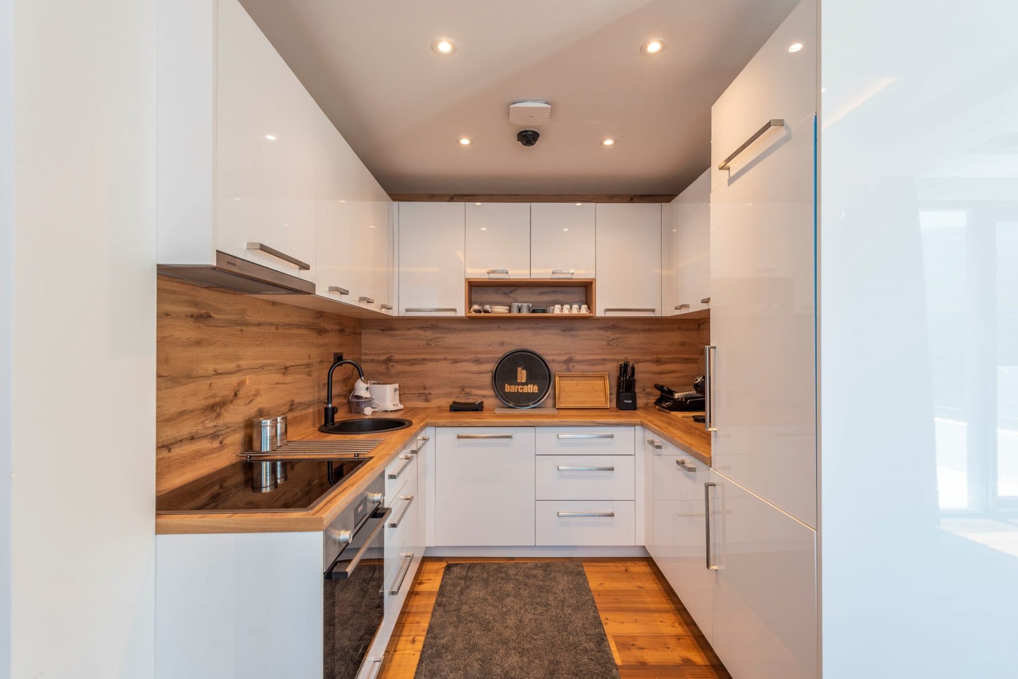 Modern white kitchen with wood finishes in a penthouse in Bečići, Montenegro: built-in appliances and stylish design.