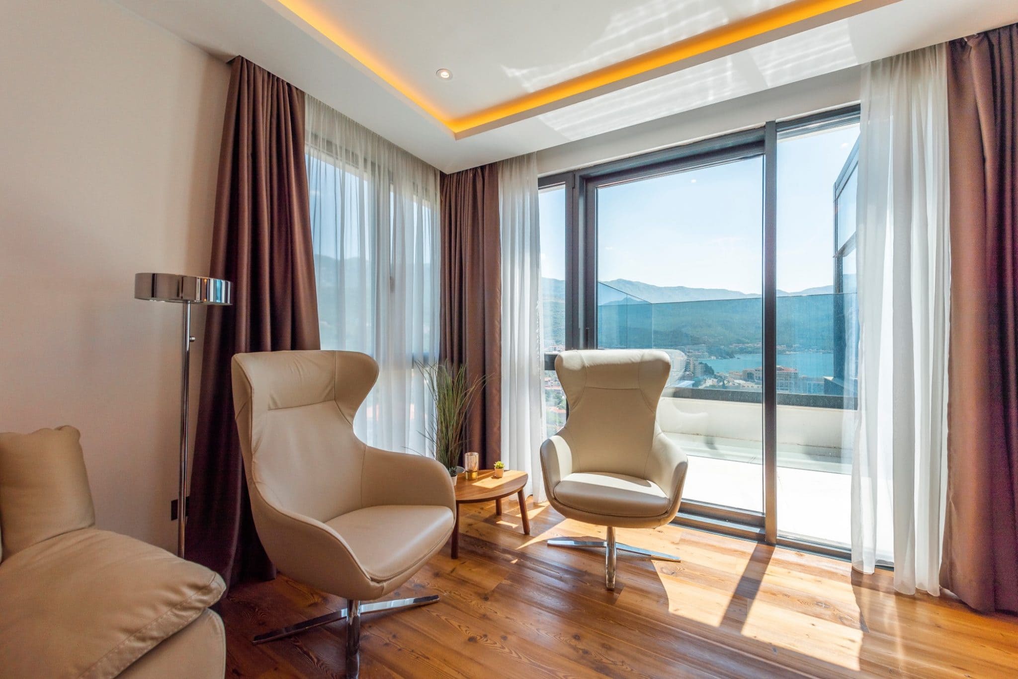 Penthouse living room in Becici, Montenegro: leather armchairs, panoramic windows with sea and mountain views, modern design.