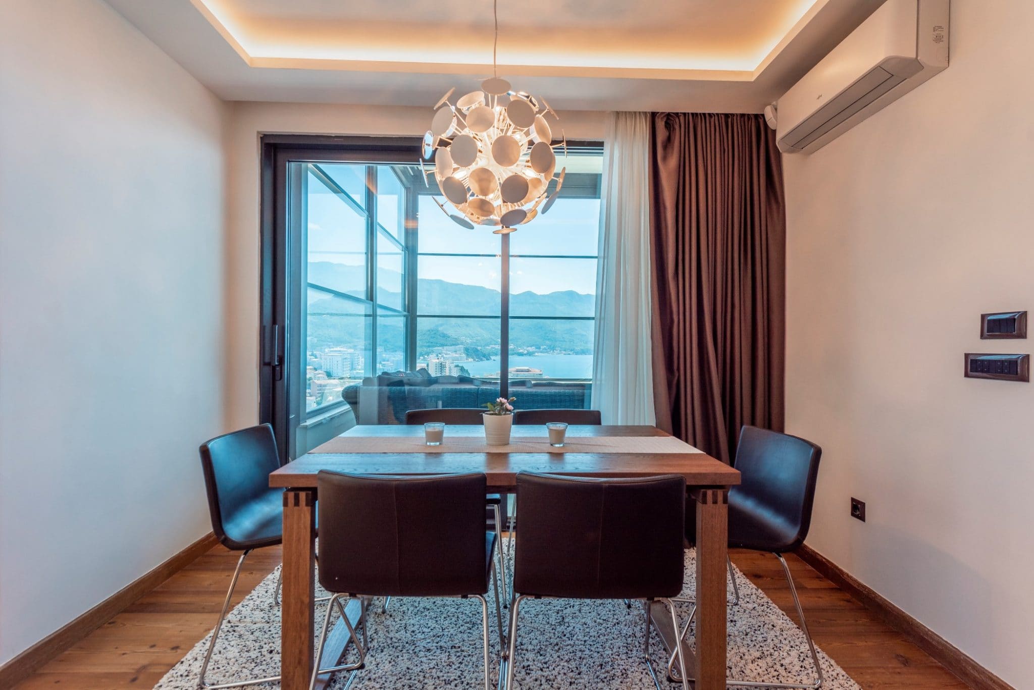Modern dining area in a penthouse in Bečići, Montenegro: wooden table, panoramic sea and mountain view.