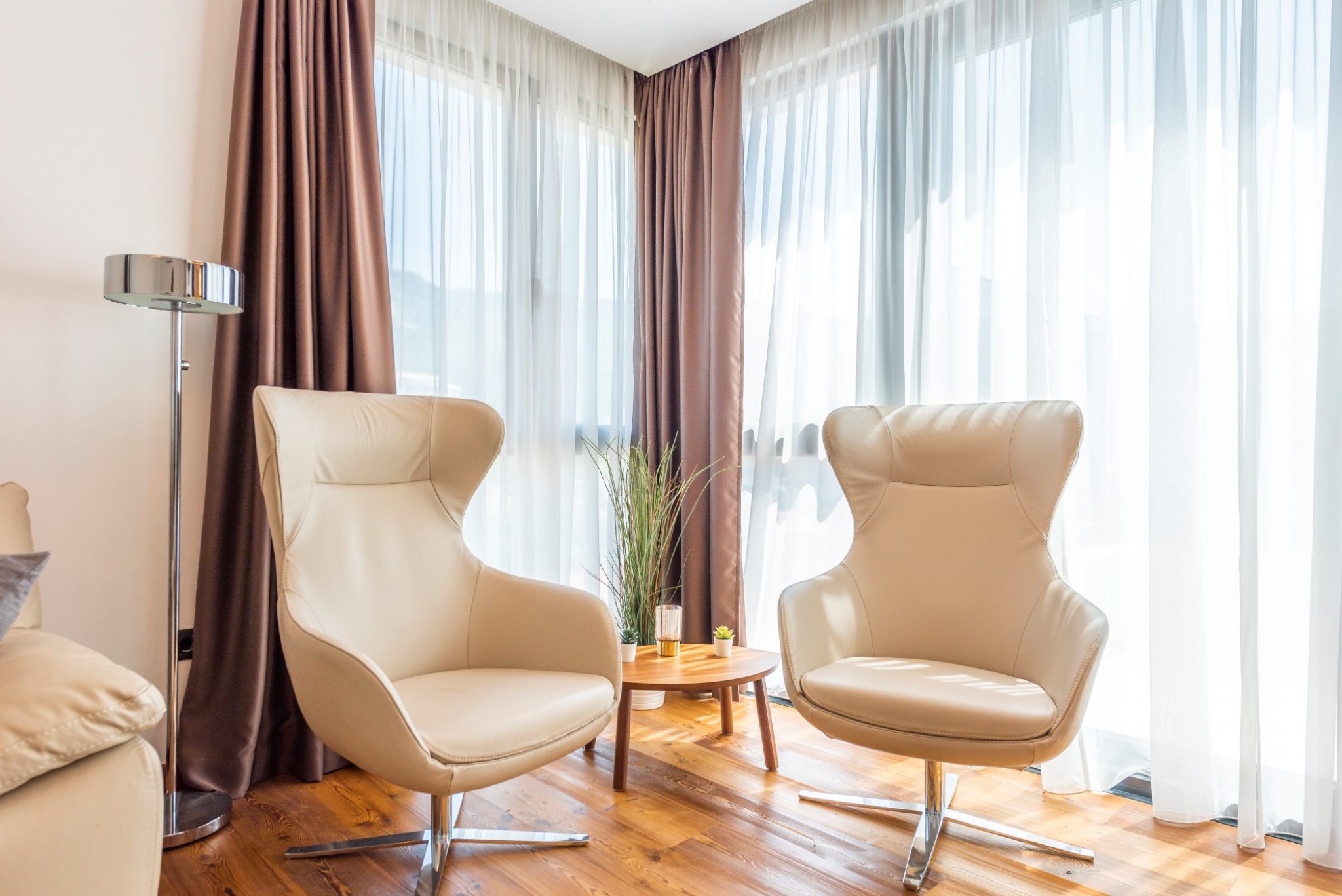 Two beige armchairs in the penthouse living room in Bečići, Montenegro, with panoramic windows and a wooden floor.