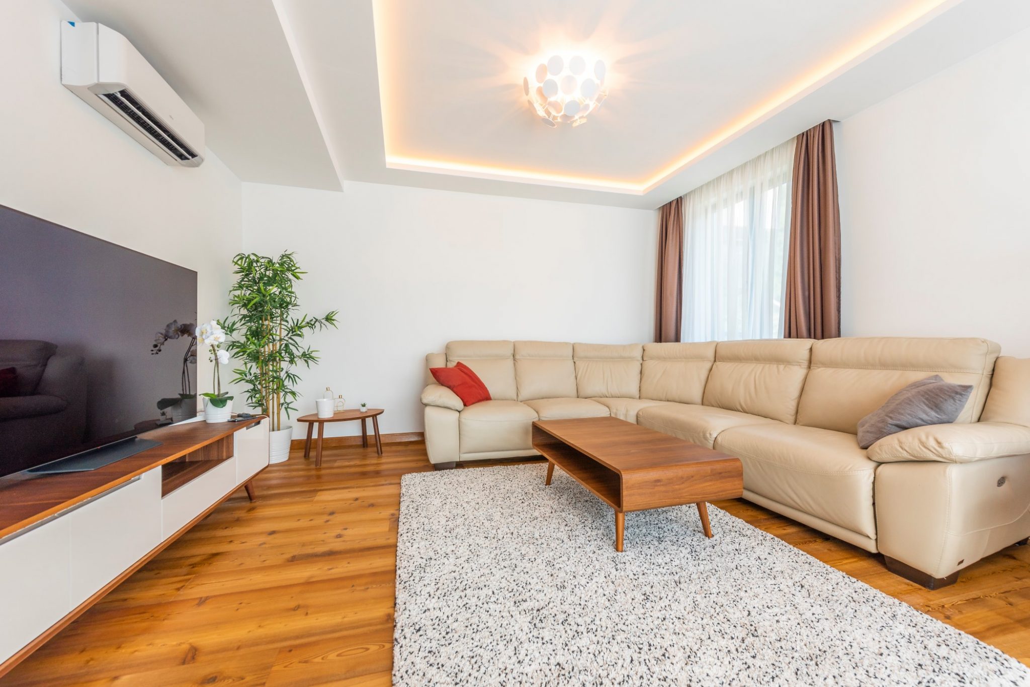 Modern living room in a penthouse in Bečići, Montenegro: leather sofa, wooden floor, TV area, and stylish lighting.