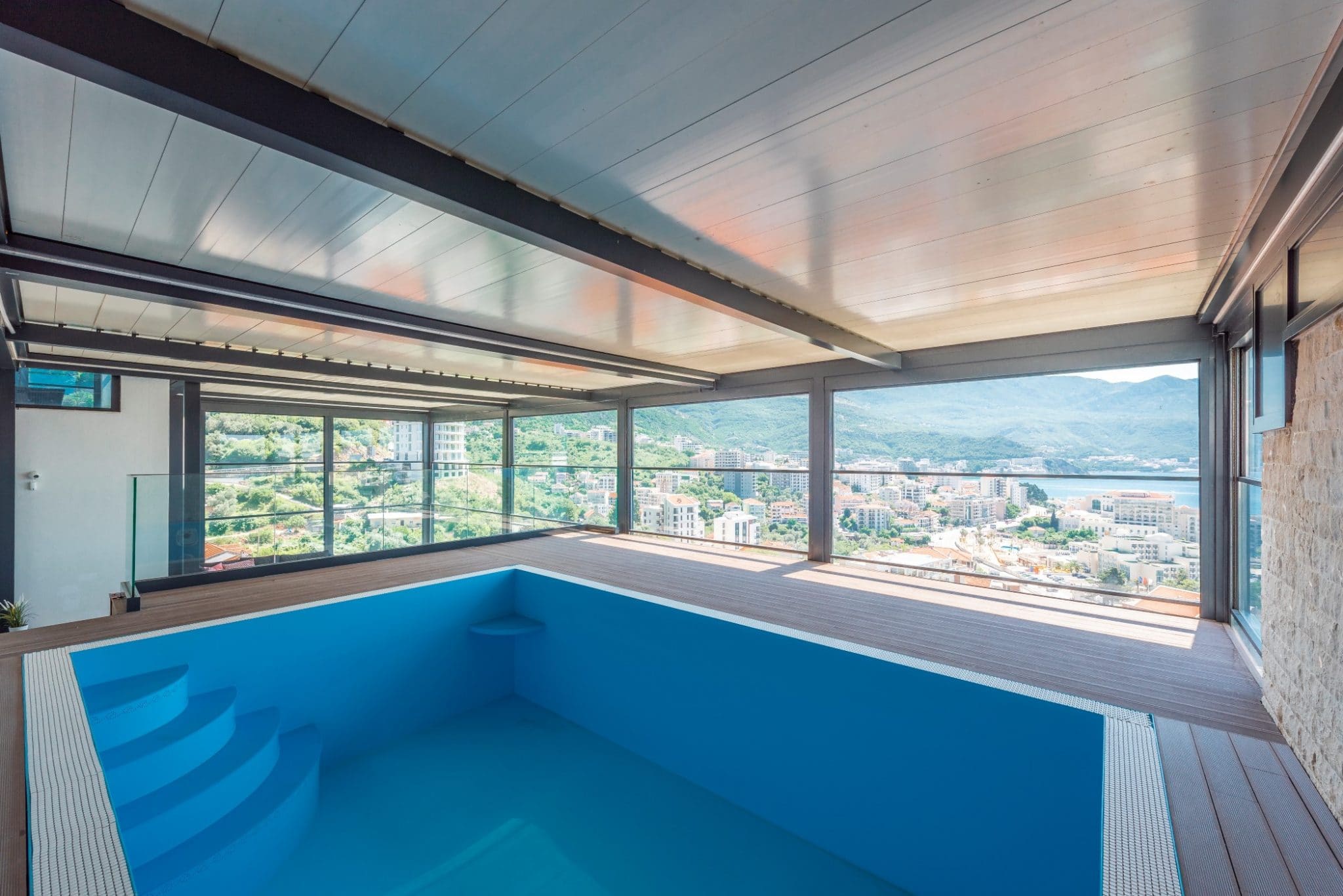 Indoor pool in a penthouse in Bečići, Montenegro, with panoramic views of the city, sea, and mountains through glass walls.