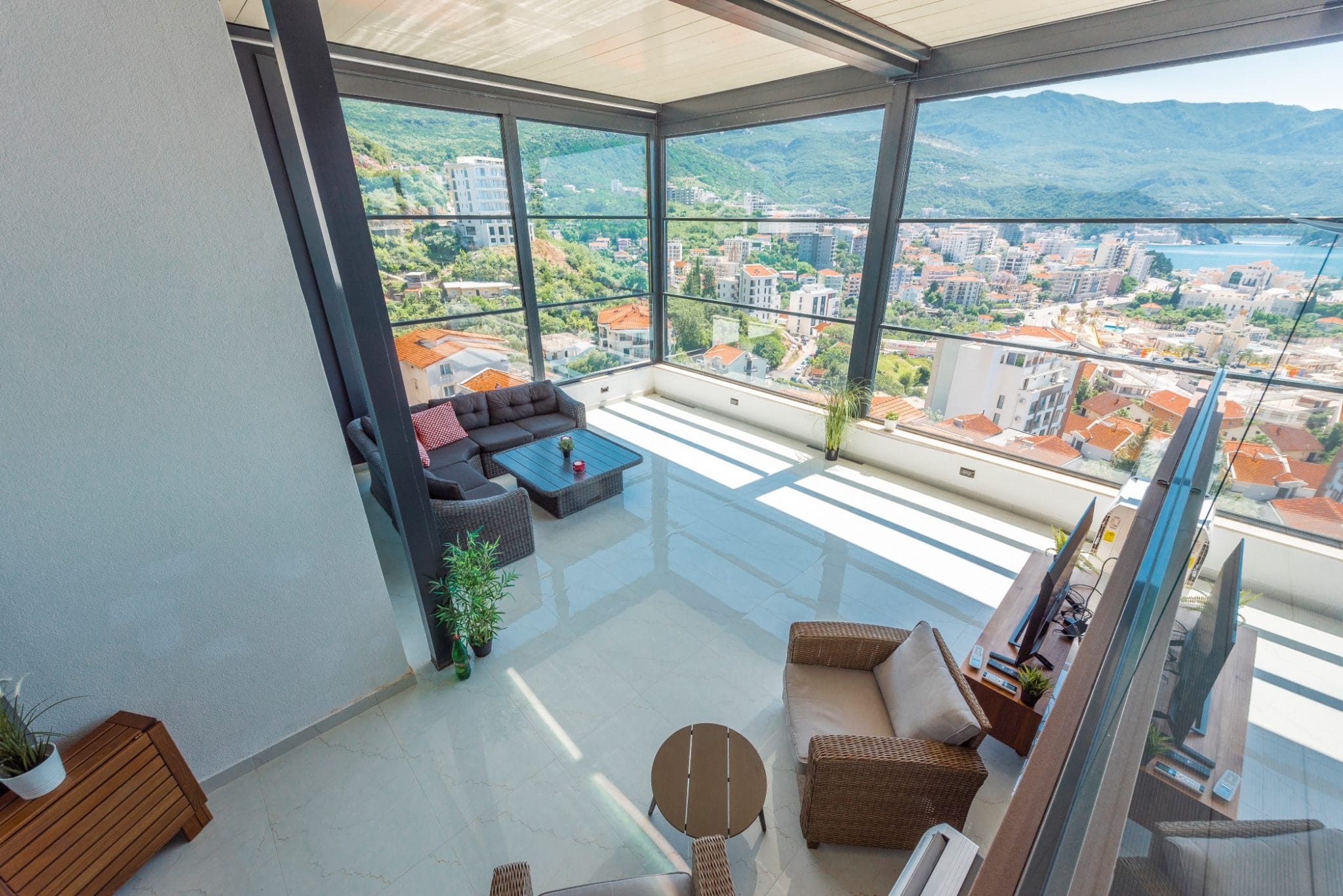 Penthouse living room in Bečići, Montenegro: panoramic windows, wicker furniture, and views of the sea and mountains.