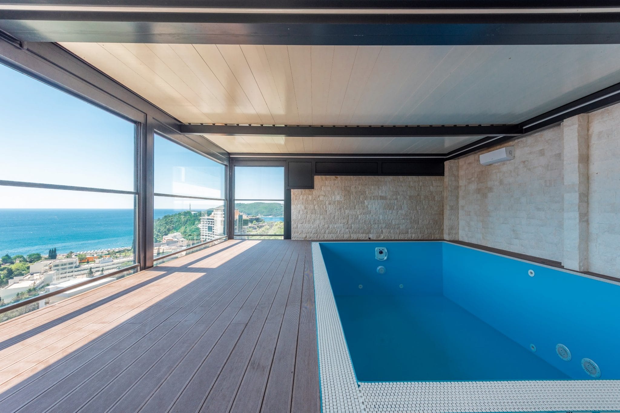 Indoor pool in a penthouse in Bečići, Montenegro: panoramic sea view, terrace with wooden decking, and stone finishes.