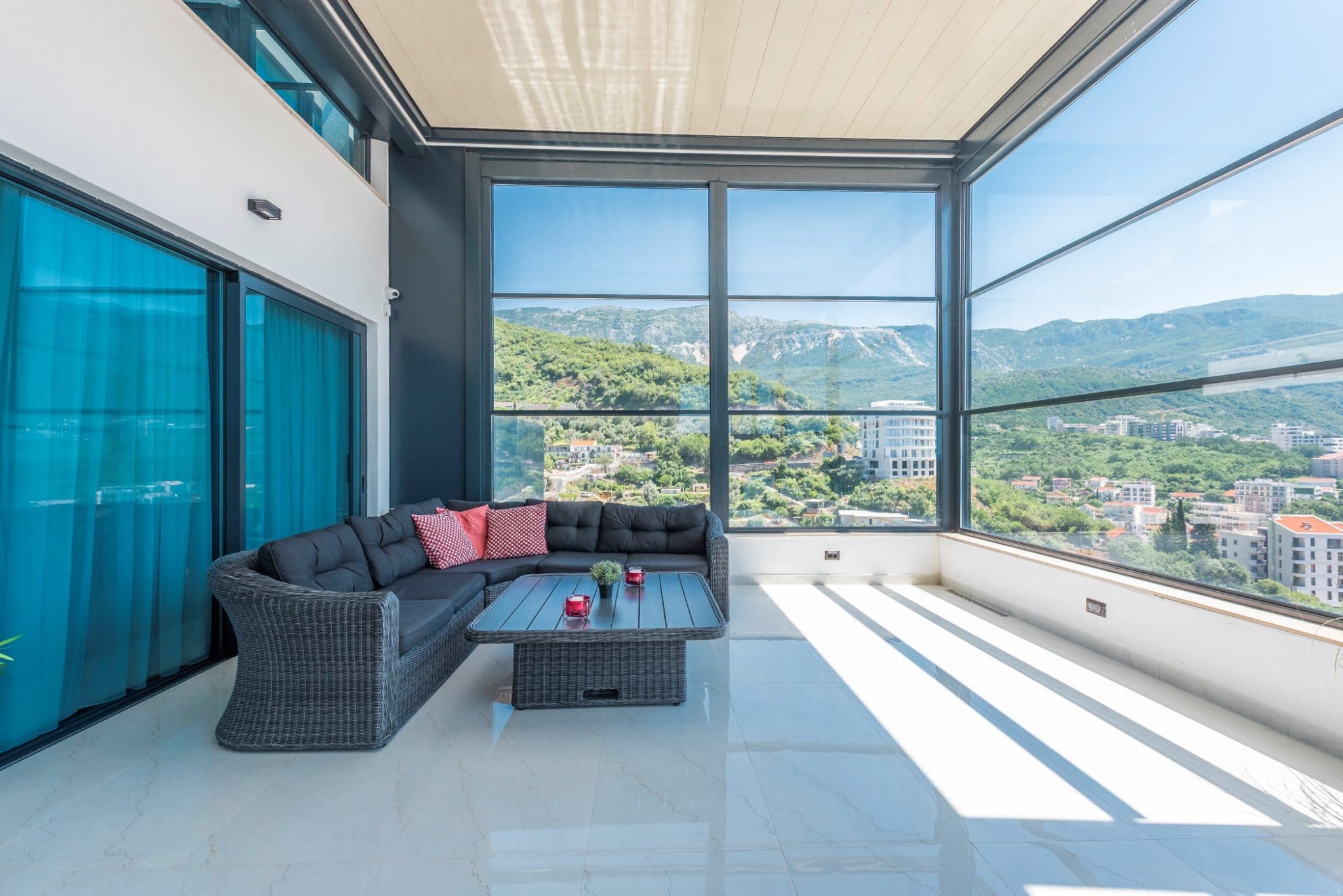 Penthouse panoramic terrace in Bečići, Montenegro: wicker furniture, light flooring, and views of the mountains and city.
